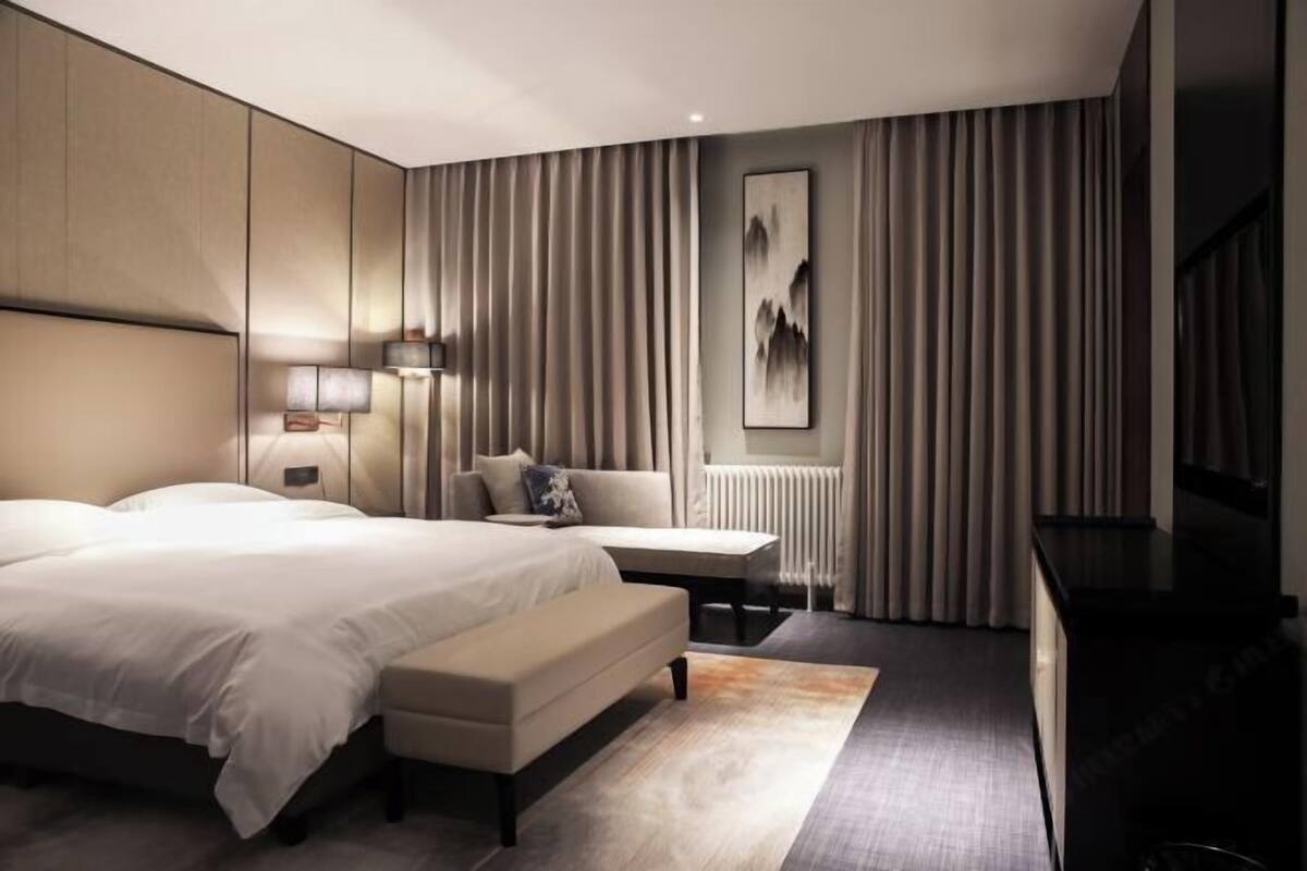 Una habitación de hotel moderna con una cama grande, una mesita de noche, un banco, un televisor montado en la pared y un radiador.