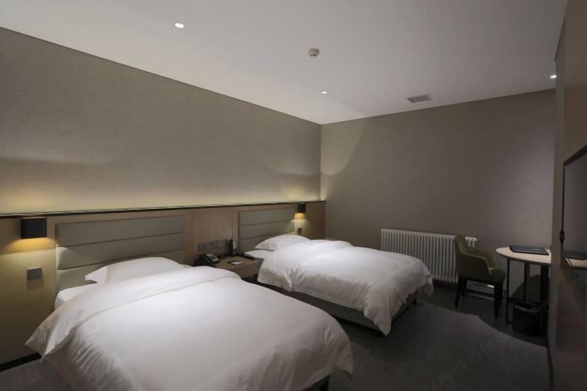 Habitación de hotel con dos camas, lámparas de noche, una mesita, una silla y un radiador.