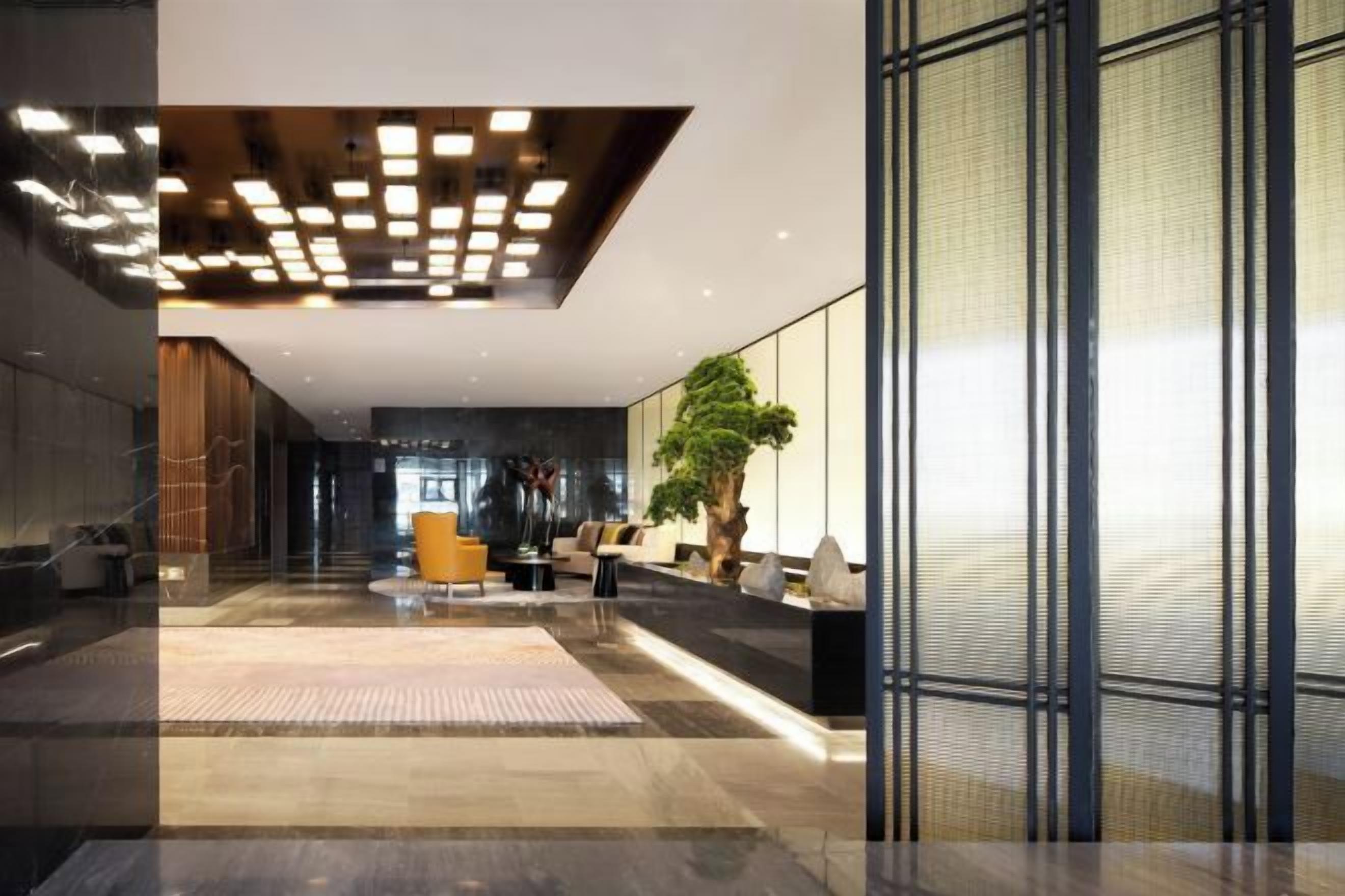 A modern lobby with a reception desk, seating area, and a large plant.