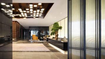 A modern lobby with a reception desk, seating area, and a large plant.