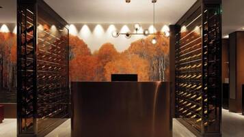 Zona de recepción con un mostrador central, estanterías para vinos a cada lado y un mural en la pared con árboles otoñales.