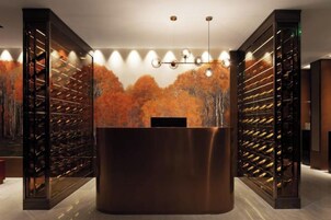 Zona de recepción con un mostrador central, estanterías para vinos a cada lado y un mural en la pared con árboles otoñales.