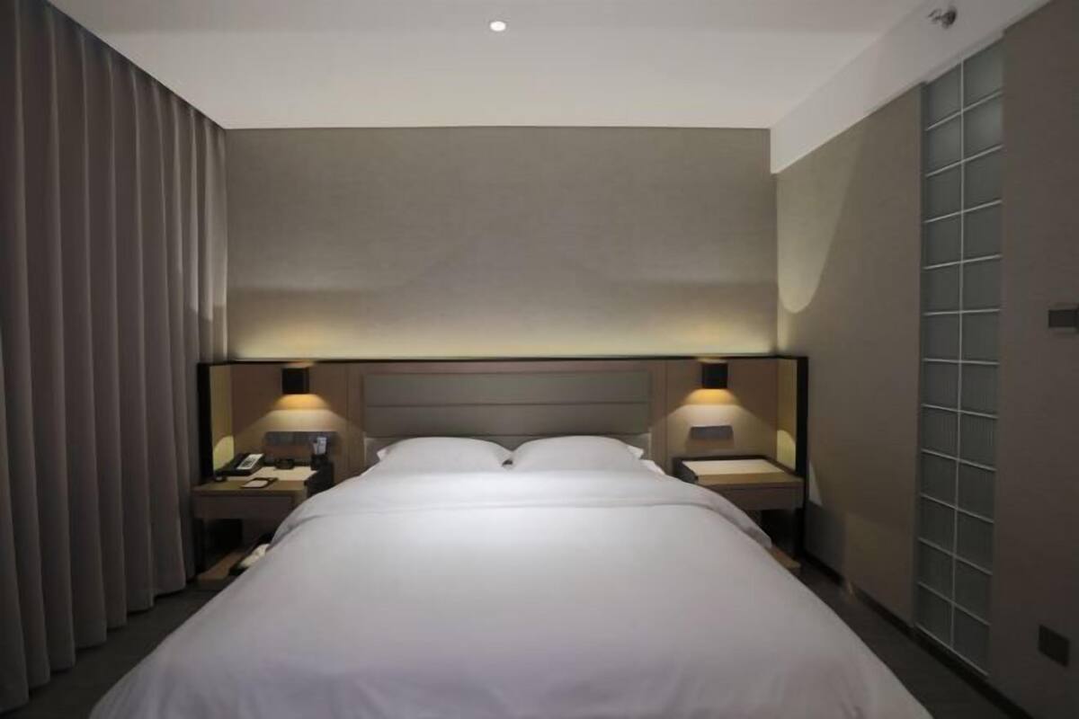 Habitación de hotel con una cama grande, dos mesitas de noche con lámparas, cabecera y una cortina a un lado.