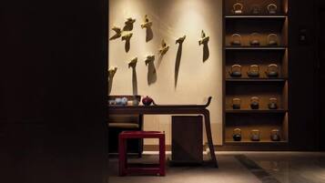 A room with a wooden bench, a small red stool, and a wall-mounted shelf with decorative items.