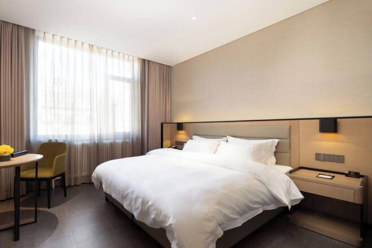 Habitación de hotel con una cama grande, mesitas de noche, un escritorio con silla y una ventana con cortinas.