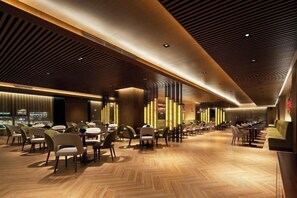 A spacious indoor area with multiple dining tables and chairs, a wooden floor, and a modern ceiling design.
