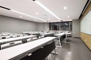 Un aula moderna con filas de escritorios, una pantalla de proyector y un amplio ventanal.
