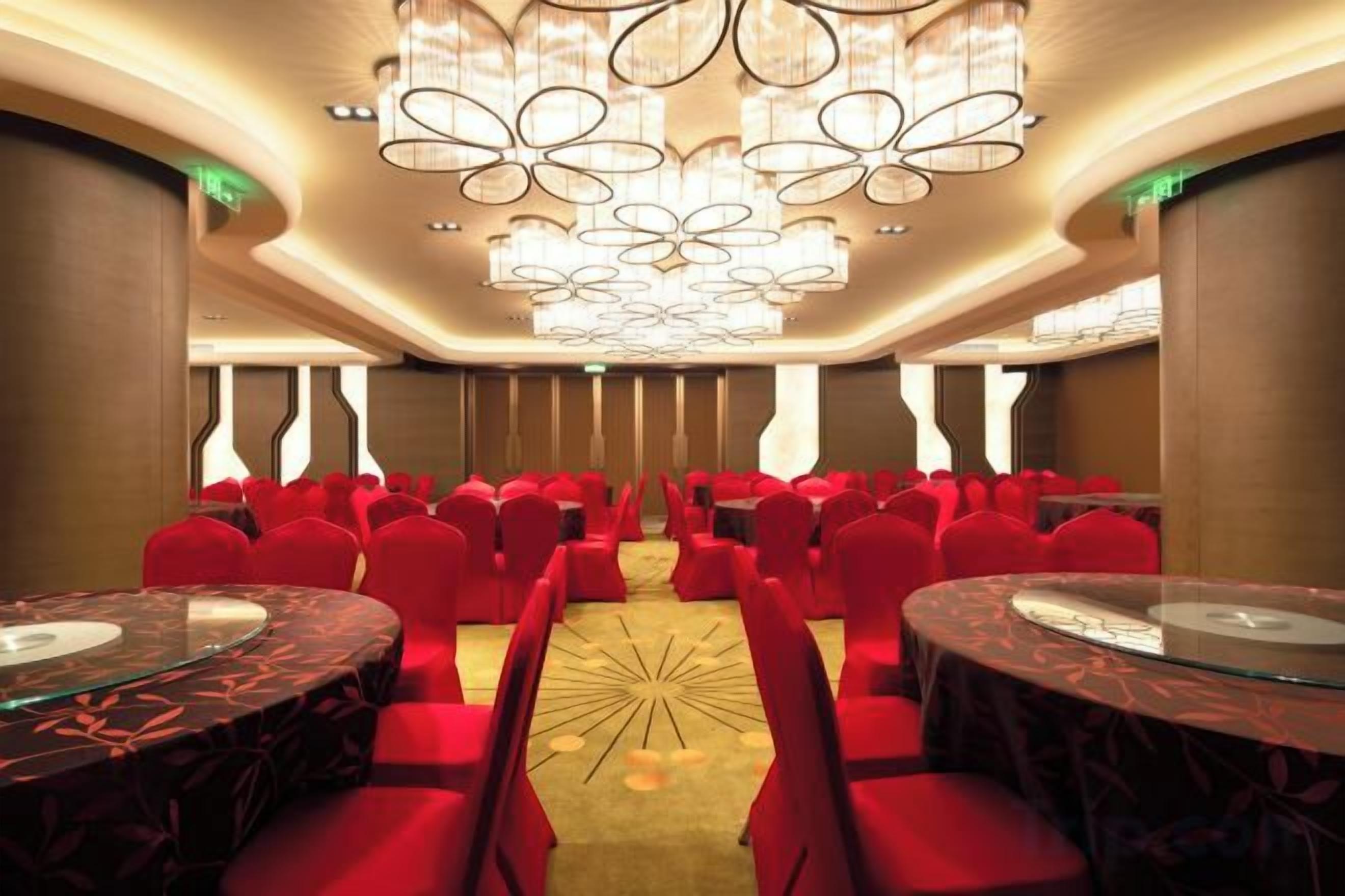 Un salón de conferencias con filas de sillas rojas, una mesa central y un moderno candelabro.