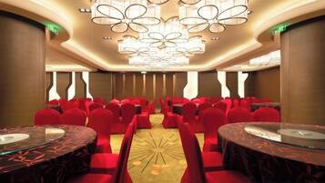 Un salón de conferencias con filas de sillas rojas, una mesa central y un moderno candelabro.