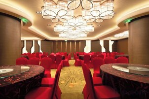 Un salón de conferencias con filas de sillas rojas, una mesa central y un moderno candelabro.