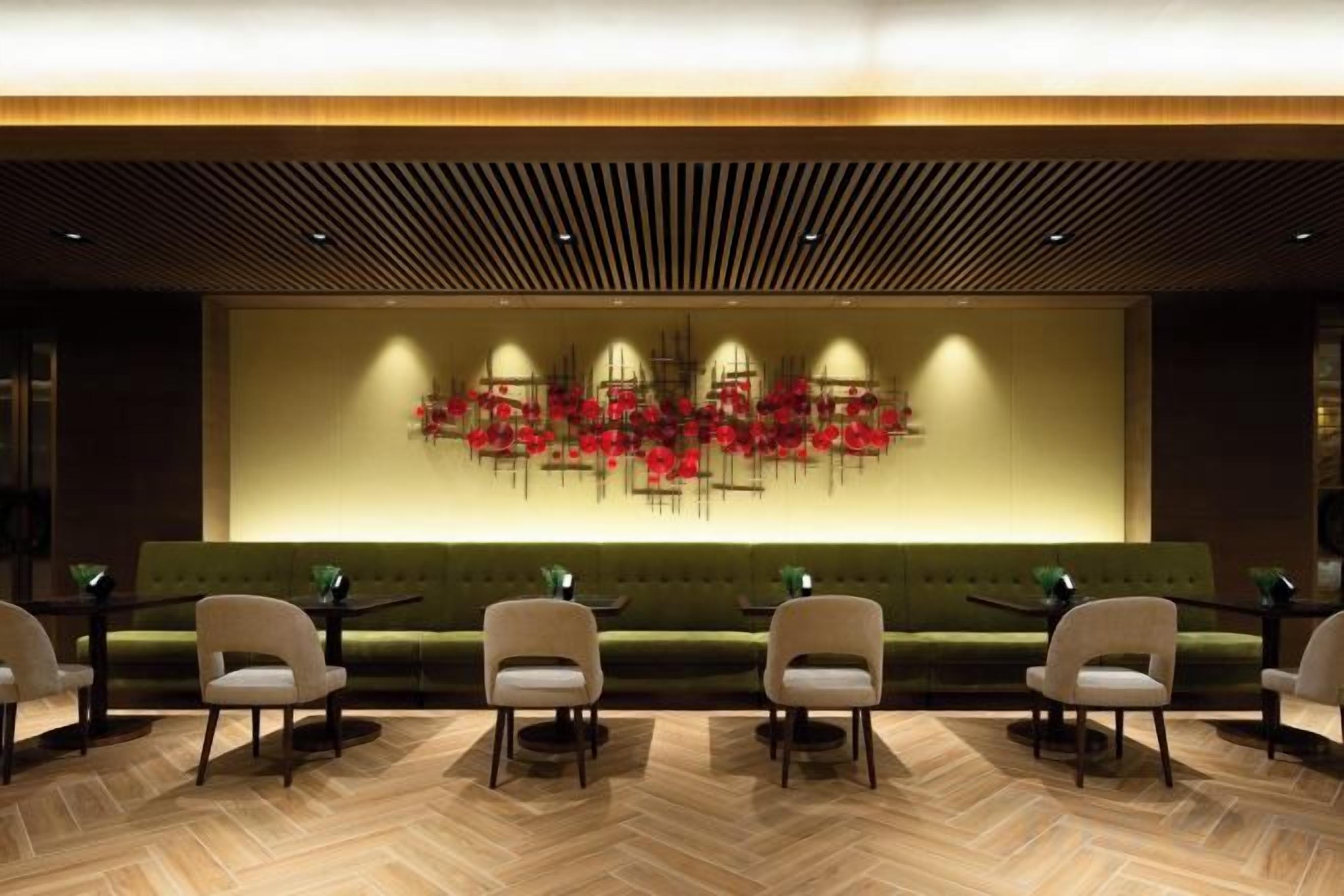 A lobby with a green sofa, white chairs, and a modern abstract art piece on the wall.