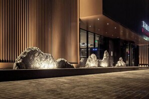 A modern building facade with vertical wooden slats, a water feature with multiple jets, and a paved walkway. - Eastern Holiday Hotel (Tonghua)