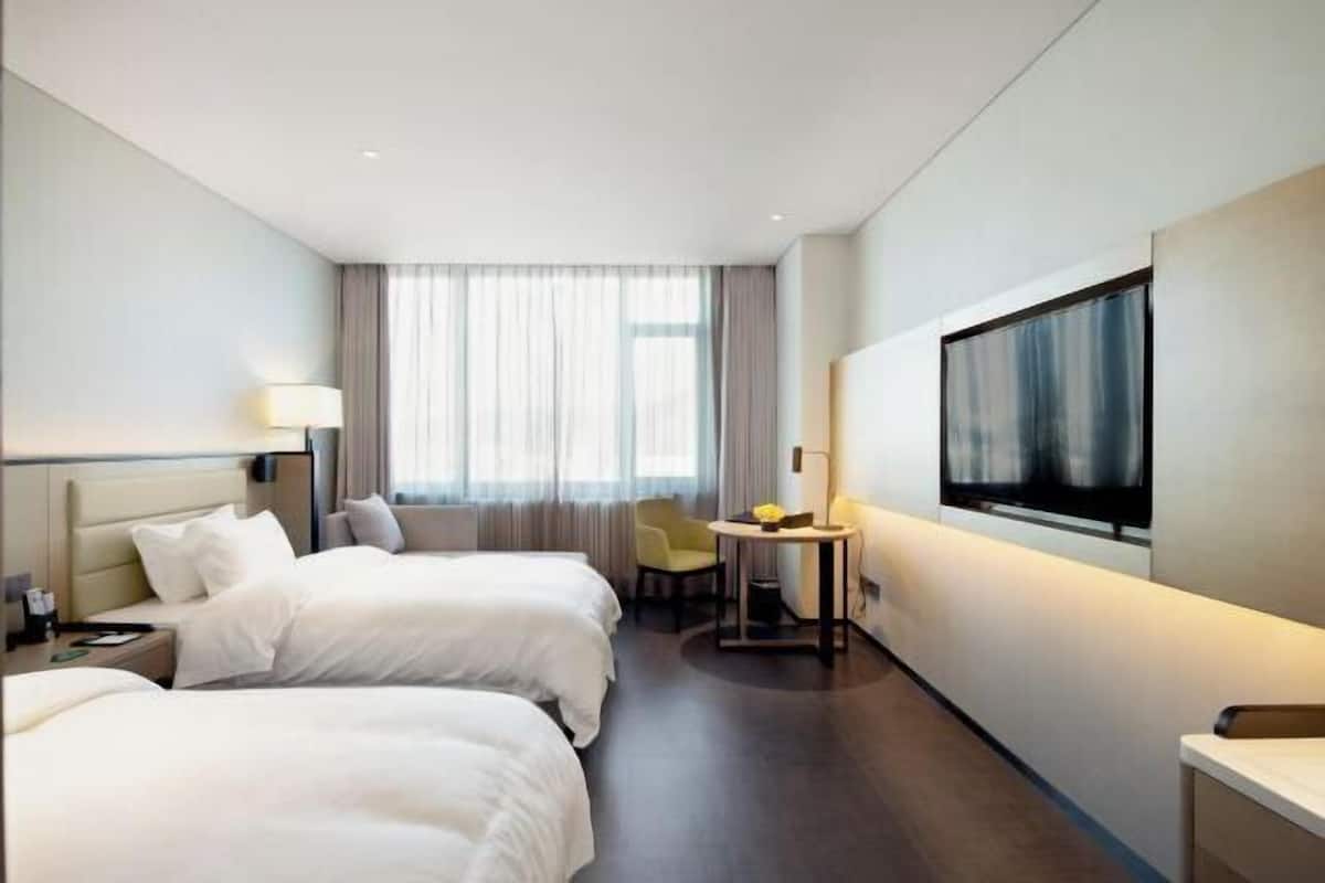 Habitación de hotel con dos camas, televisión, escritorio con silla y ventana con cortinas.