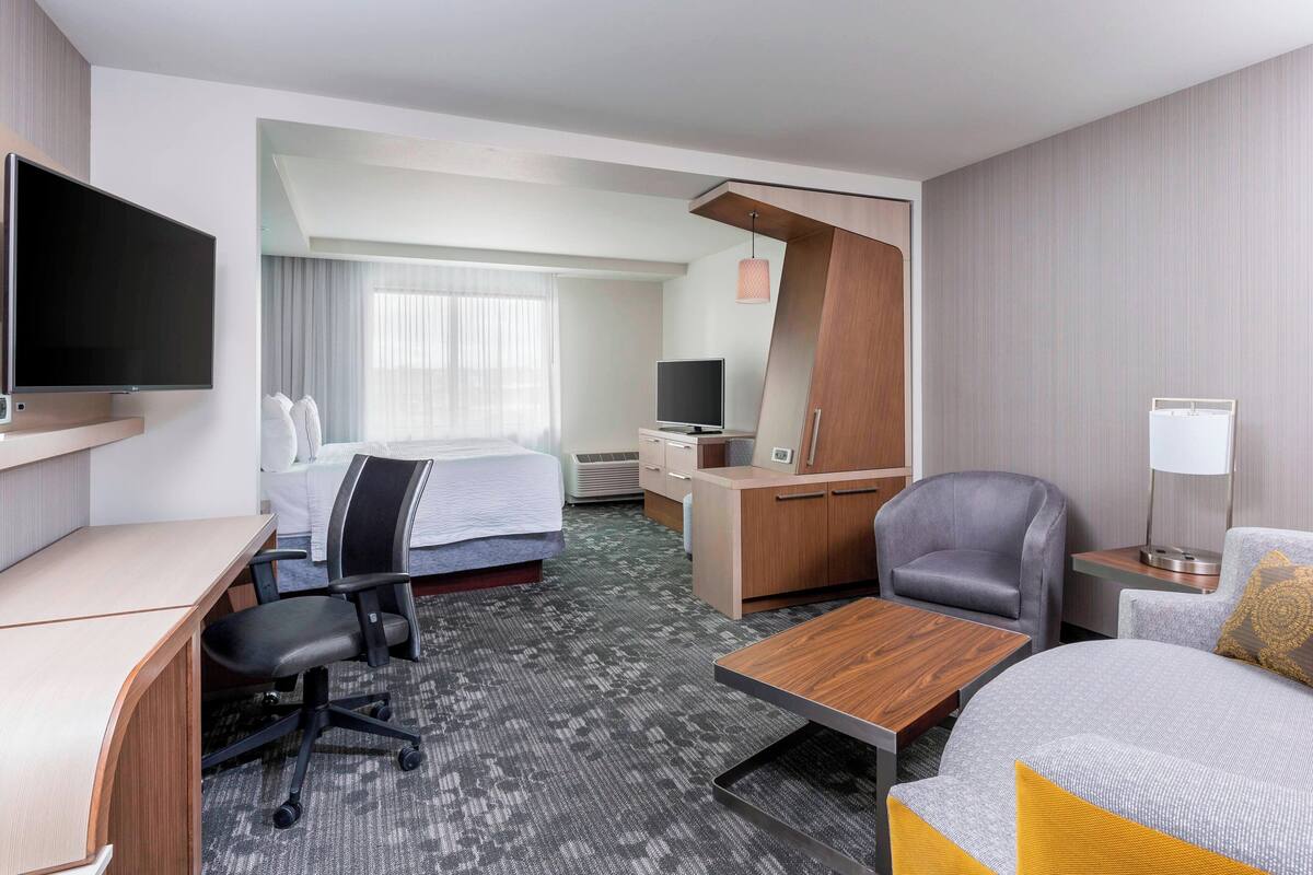 Una habitación de hotel con cama, escritorio, silla, televisor y sofá.