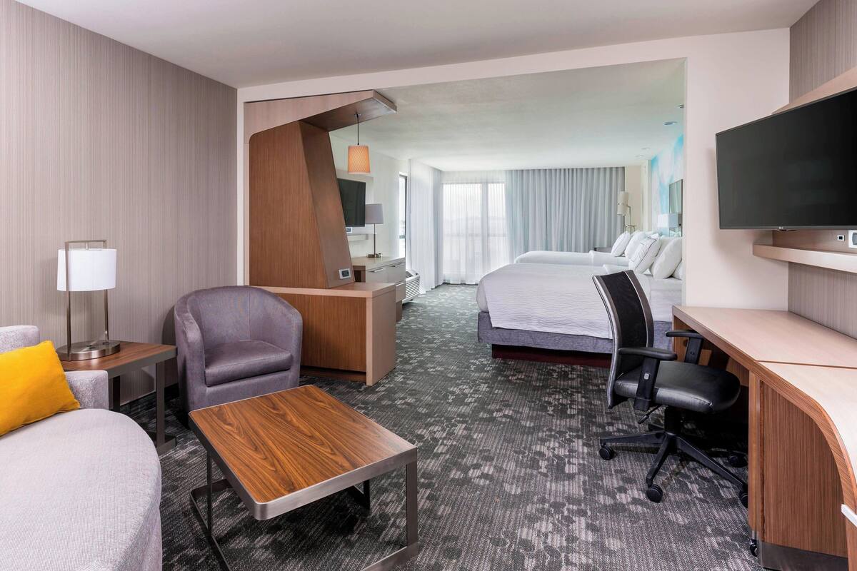 Una habitación de hotel con cama, escritorio, silla, televisor y lámpara.