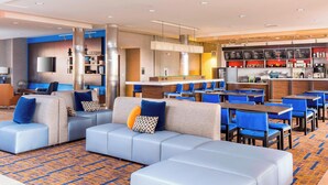 Een moderne hotellobby met een hoekbank, blauwe stoelen, een bar en een flatscreen-tv.