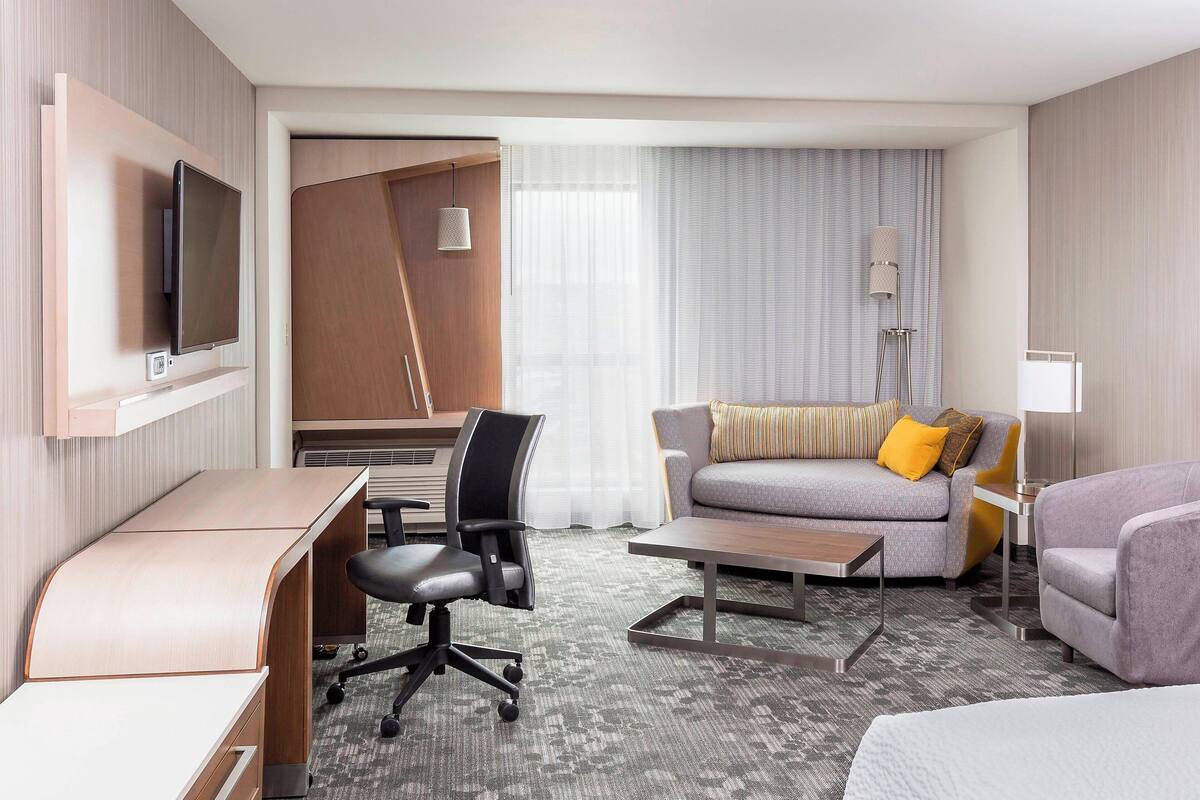 Una habitación de hotel con escritorio, sofá, cama y televisor en la pared.