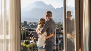 A couple embracing on a balcony with a mountain view. - alpenhotel Kaiserfels (Sankt Johann in Tirol)