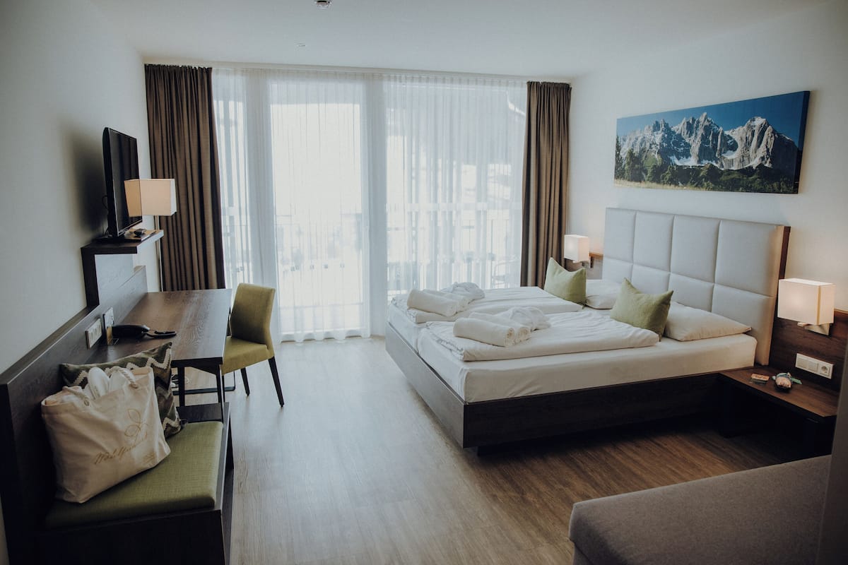 A hotel room with a bed, a desk, a chair, a TV, and a painting on the wall.