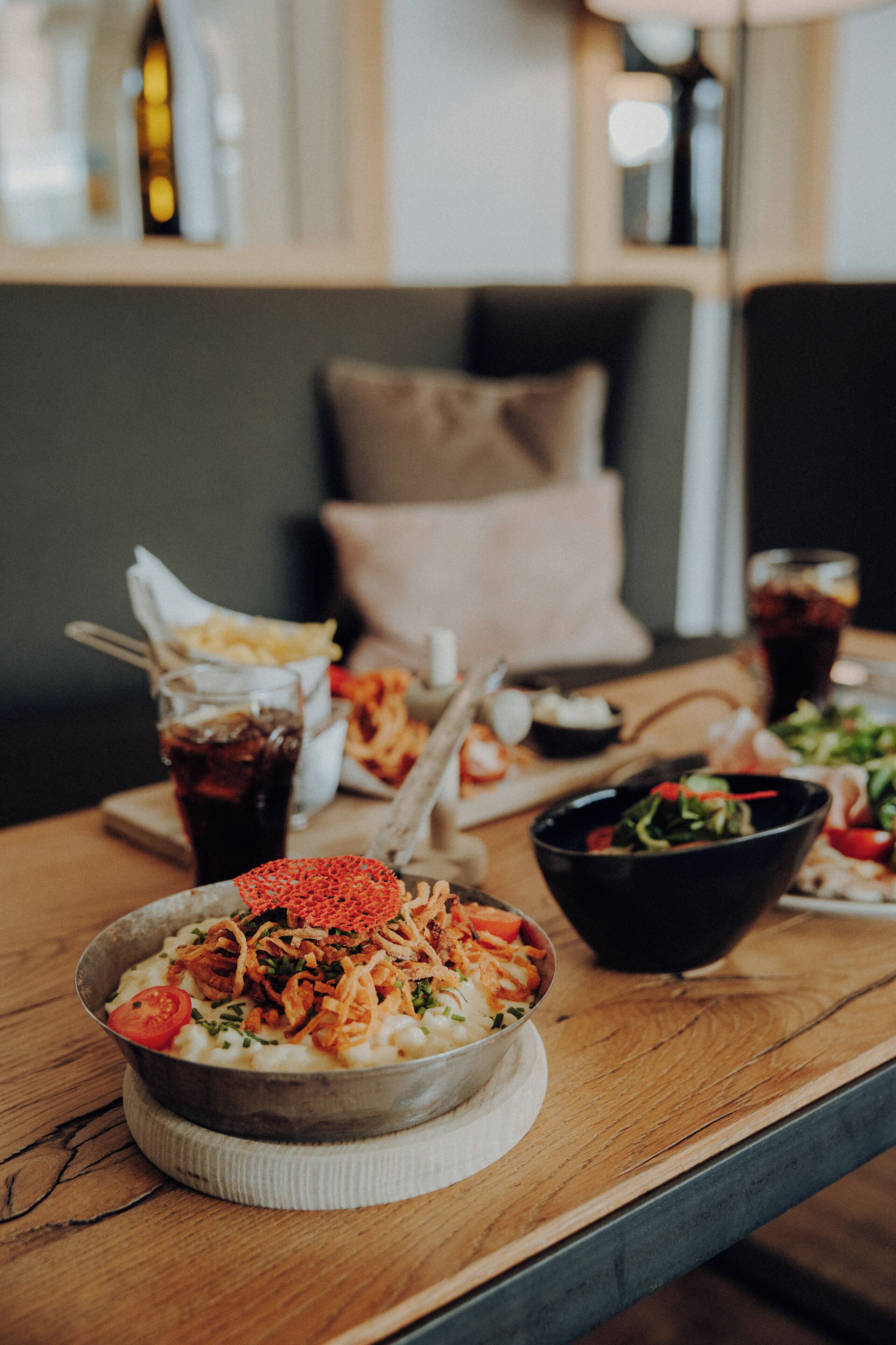Een eettafel met diverse gerechten, waaronder een saladeschaal, een pastaschotel en een glas frisdrank.