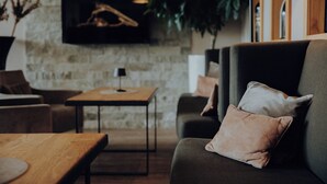 A modern living room with a stone wall, a flat-screen TV, a wooden coffee table, and a sofa with cushions. - alpenhotel Kaiserfels (Sankt Johann in Tirol)