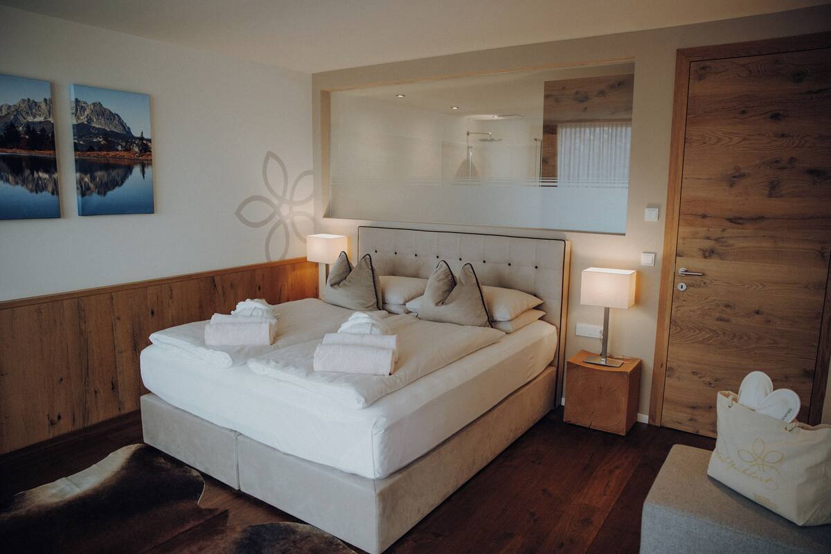 A neatly made bed with towels, a wooden headboard, bedside lamps, and a wooden door.