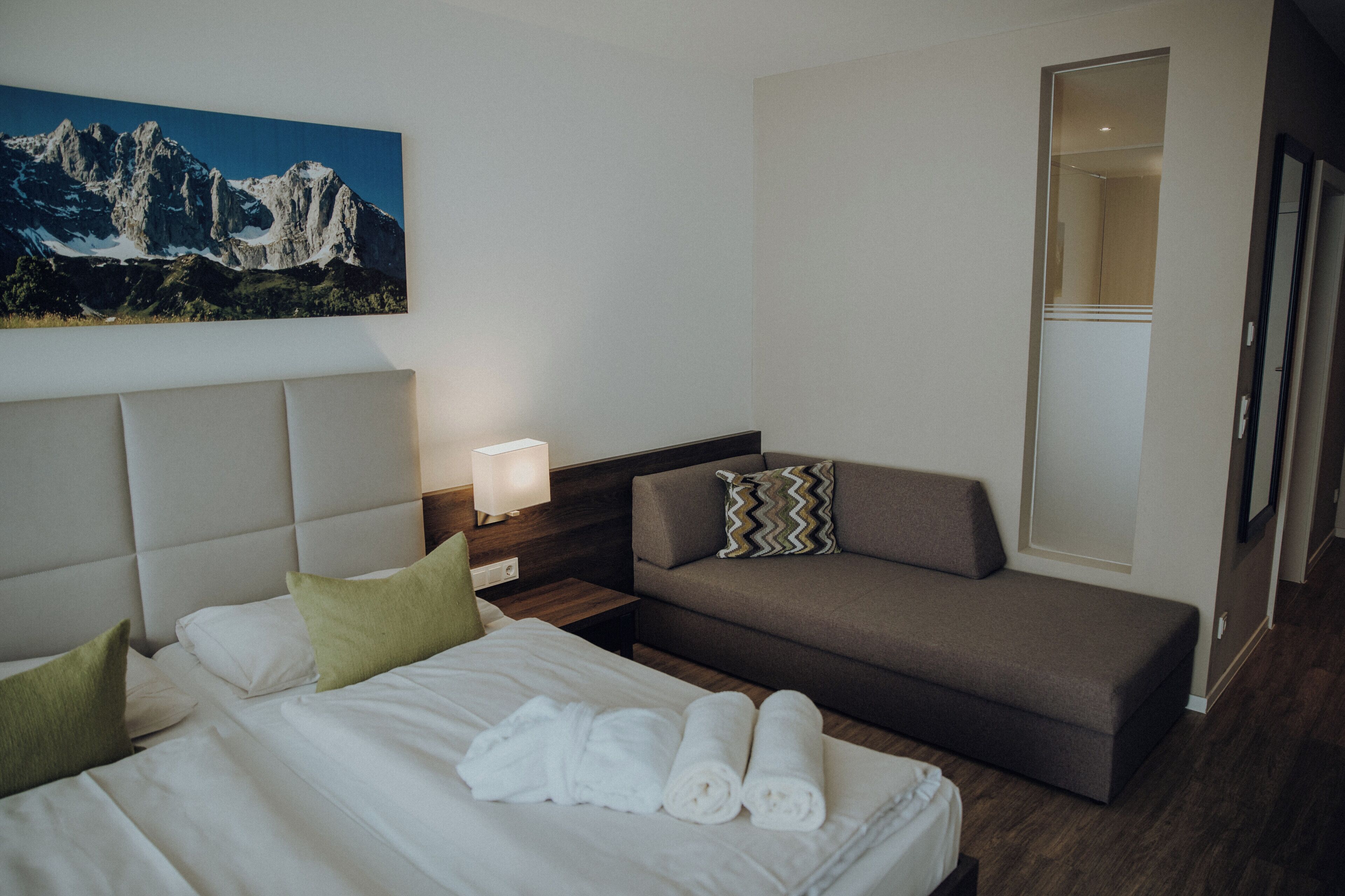 Ein Hotelzimmer mit einem Bett, einem Schlafsofa, einem Nachttisch mit Lampe und einem Bergpanorama.