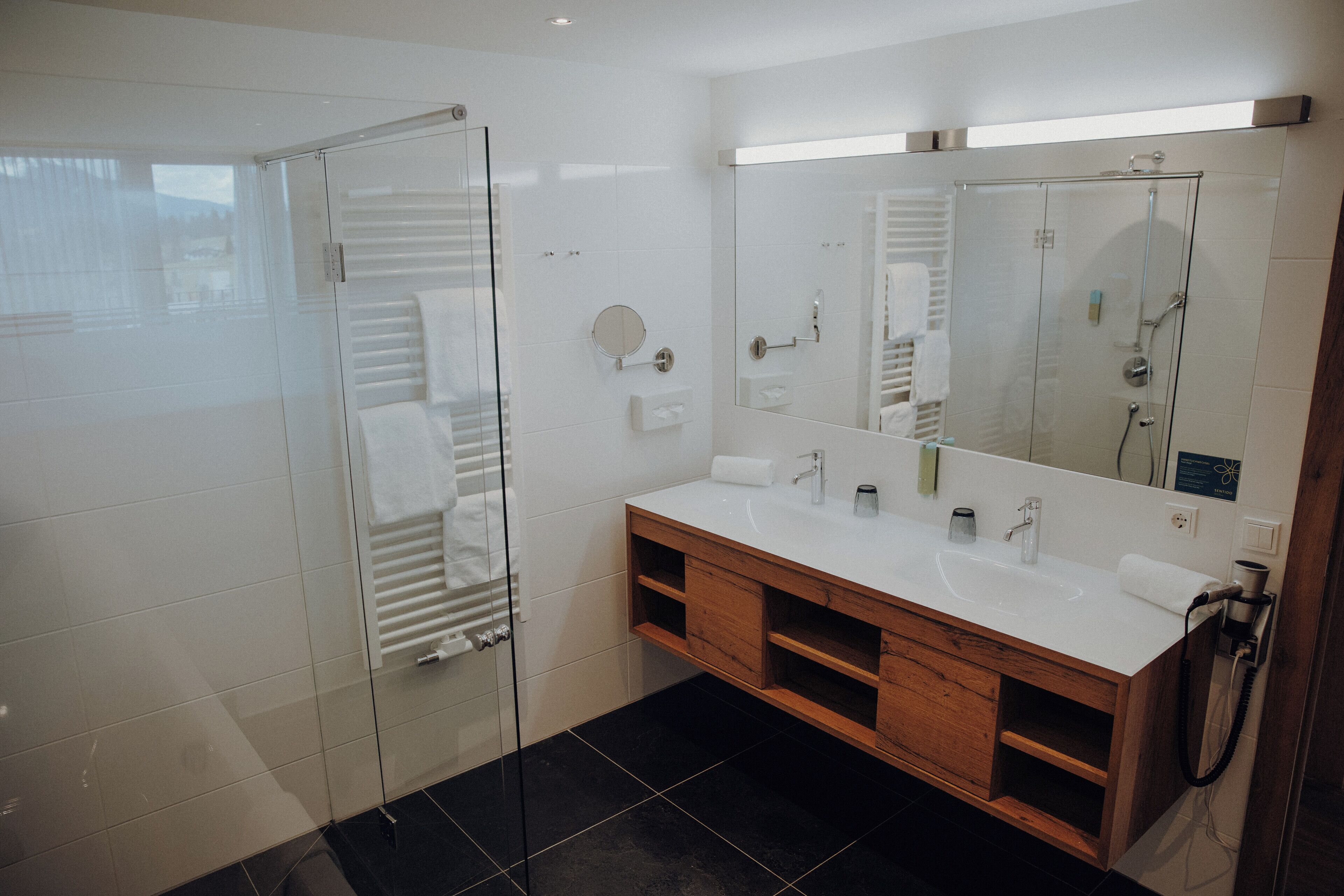 Un baño moderno con cabina de ducha de vidrio, lavamanos blanco y tocador de madera.
