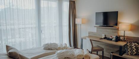 A hotel room with two beds, a desk, a television, and a view of the city.