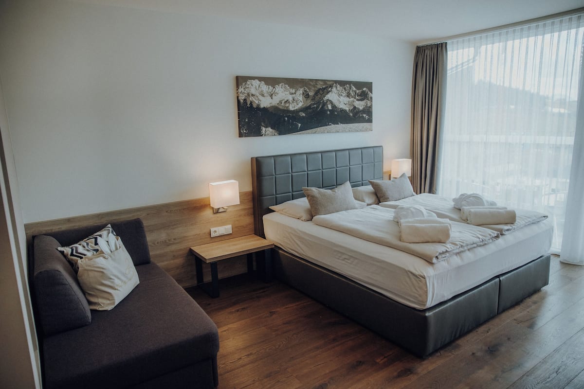 A modern hotel room with a large bed, a sofa, a nightstand, and a wall-mounted painting.