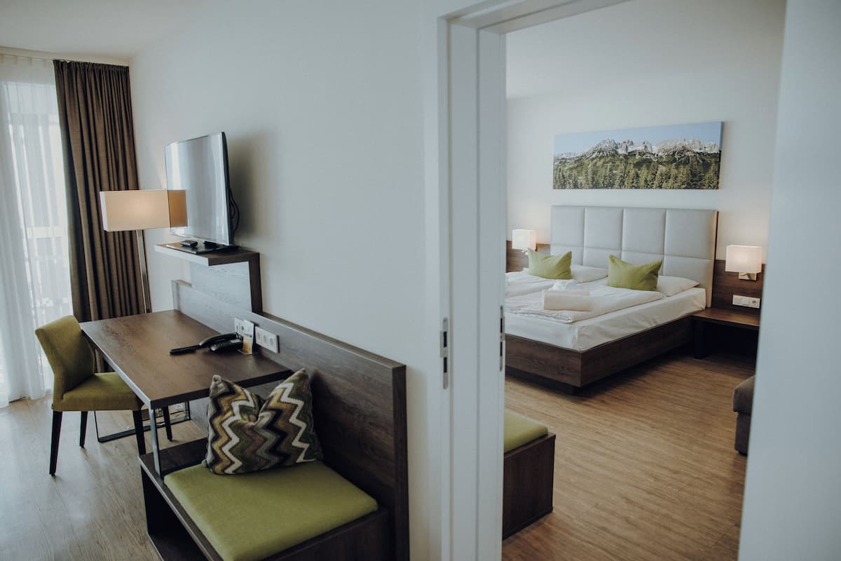 A hotel room with a bed, a desk, a chair, a television, and a painting on the wall.