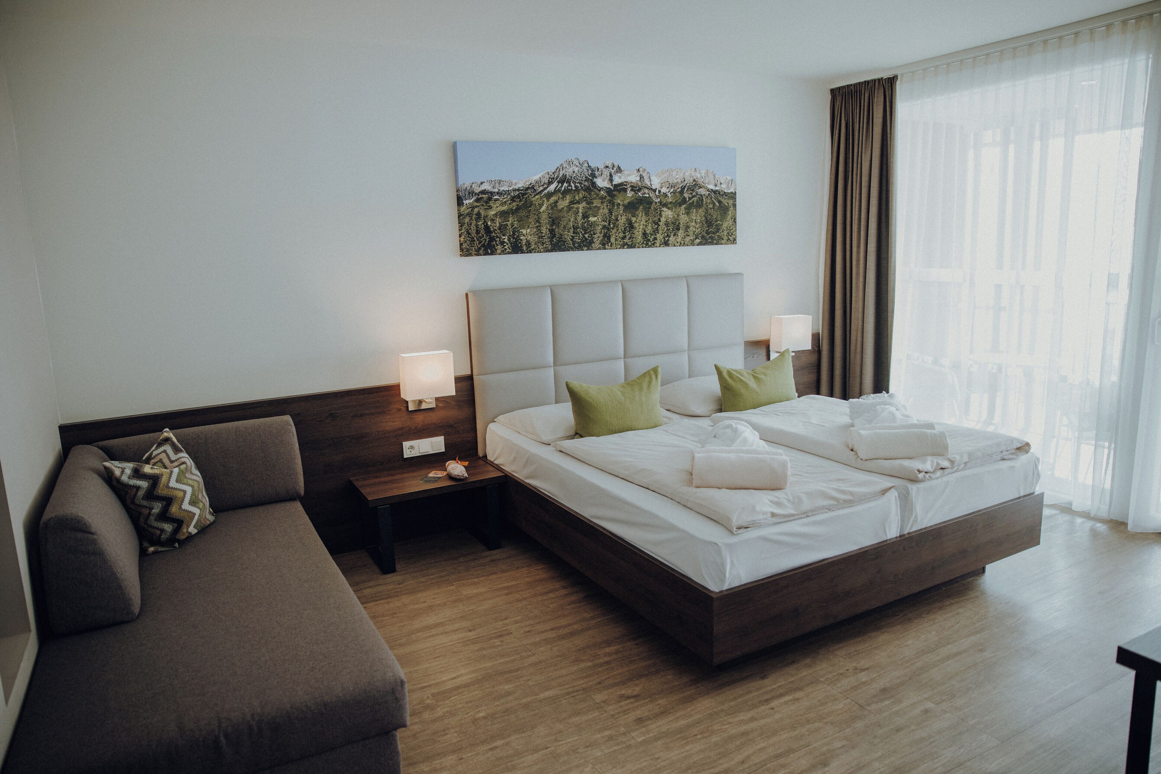 Une chambre d’hôtel moderne avec un grand lit, un canapé, une table de chevet et un tableau accroché au mur.