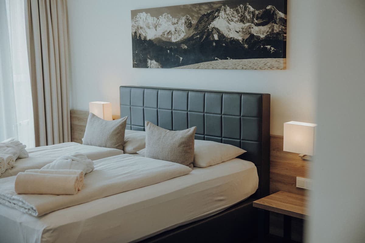 A hotel room with a large bed, two bedside lamps, and a mountain landscape painting on the wall.