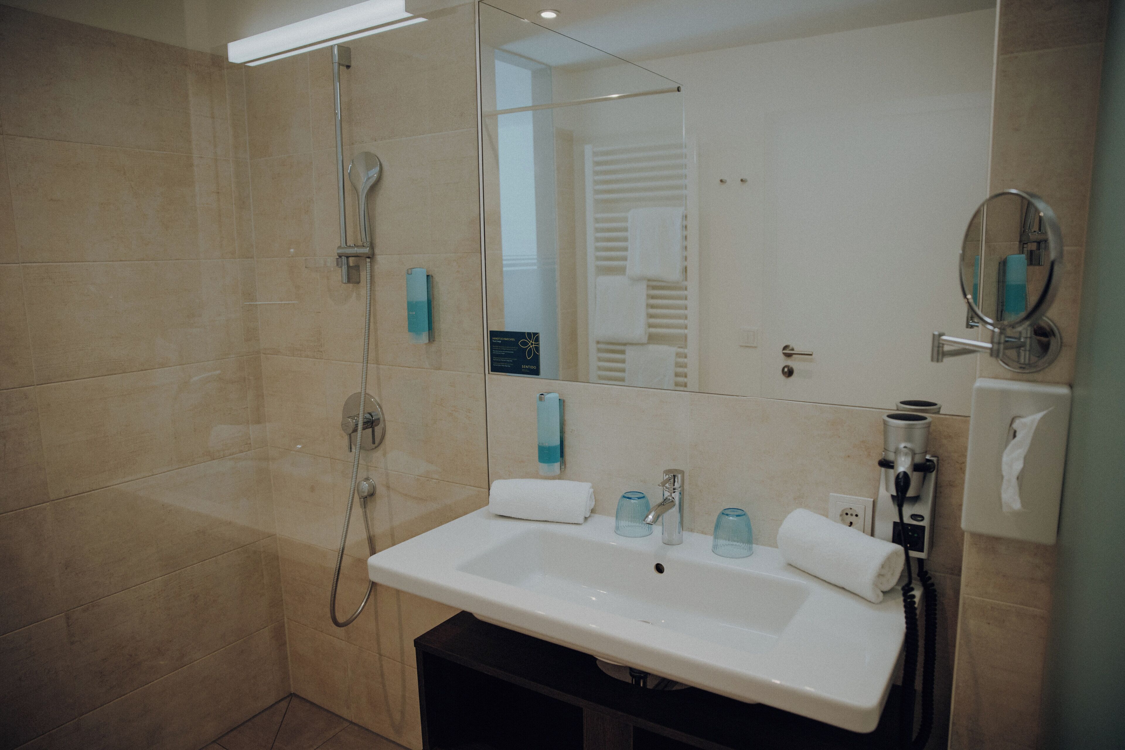 A modern bathroom with a large sink, a glass shower enclosure, and a mirror with a round frame.