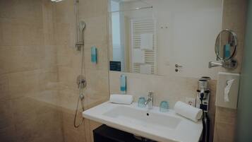 A modern bathroom with a large sink, a glass shower enclosure, and a mirror with a round frame.