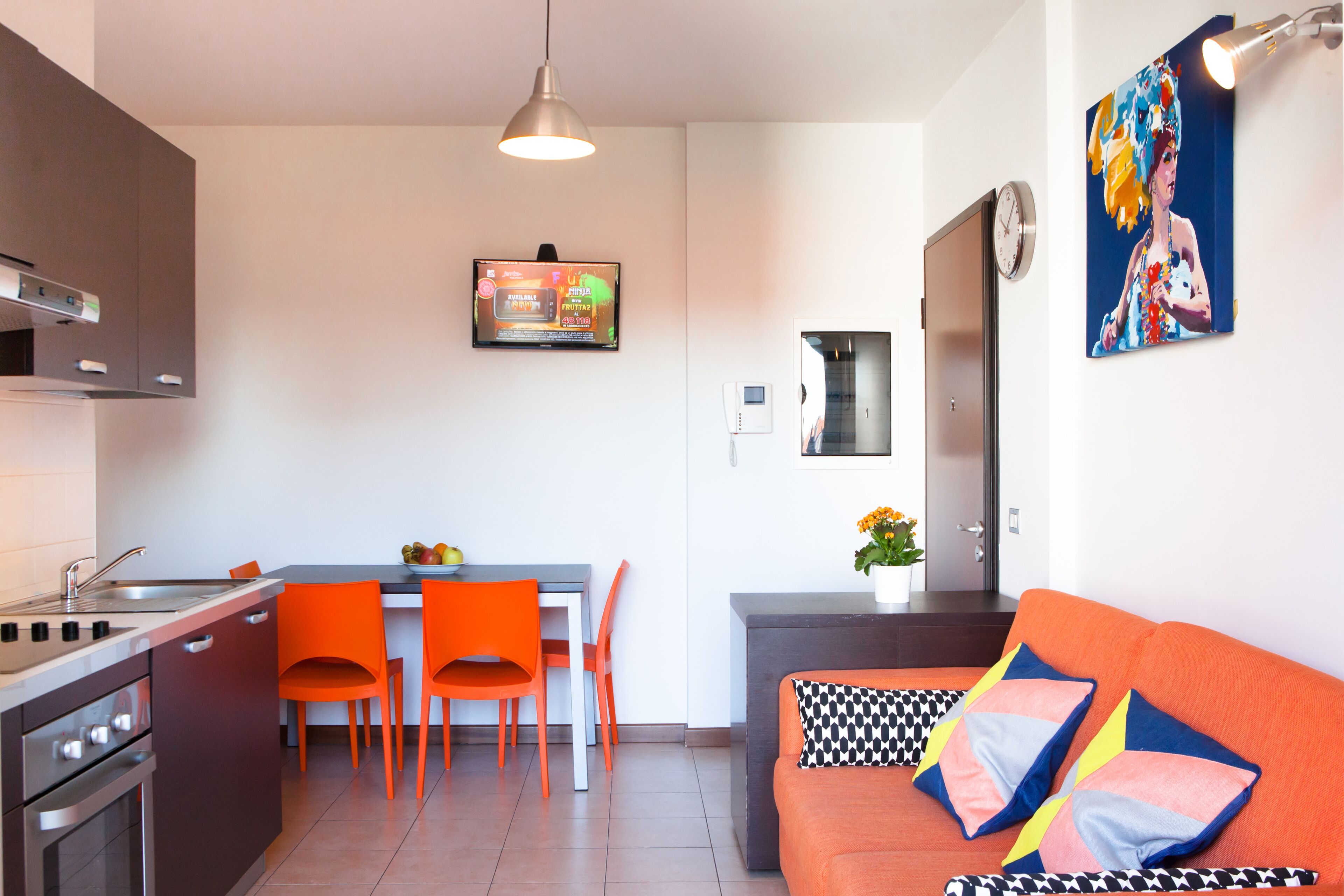 A modern kitchen with a dining area, a sofa with patterned cushions, and a painting on the wall.