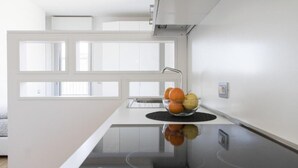 Eine moderne Küche mit Glaskochfeld, Obstschale auf der Arbeitsfläche und einem Fenster mit Jalousien.