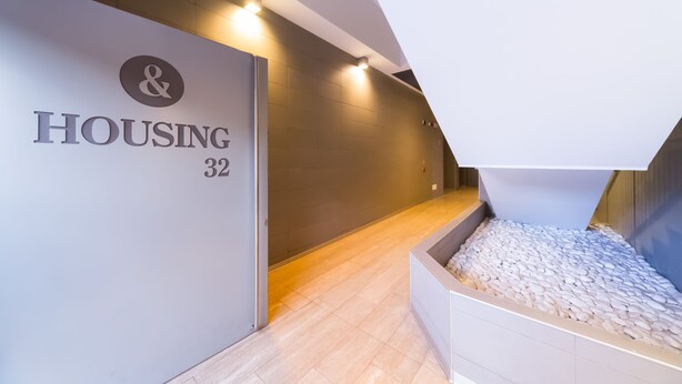 Ein moderner Flur mit einem Schild, das „HOUSING 32“ zeigt, und einem kleinen Pflanzgefäß mit weißen Kieselsteinen.