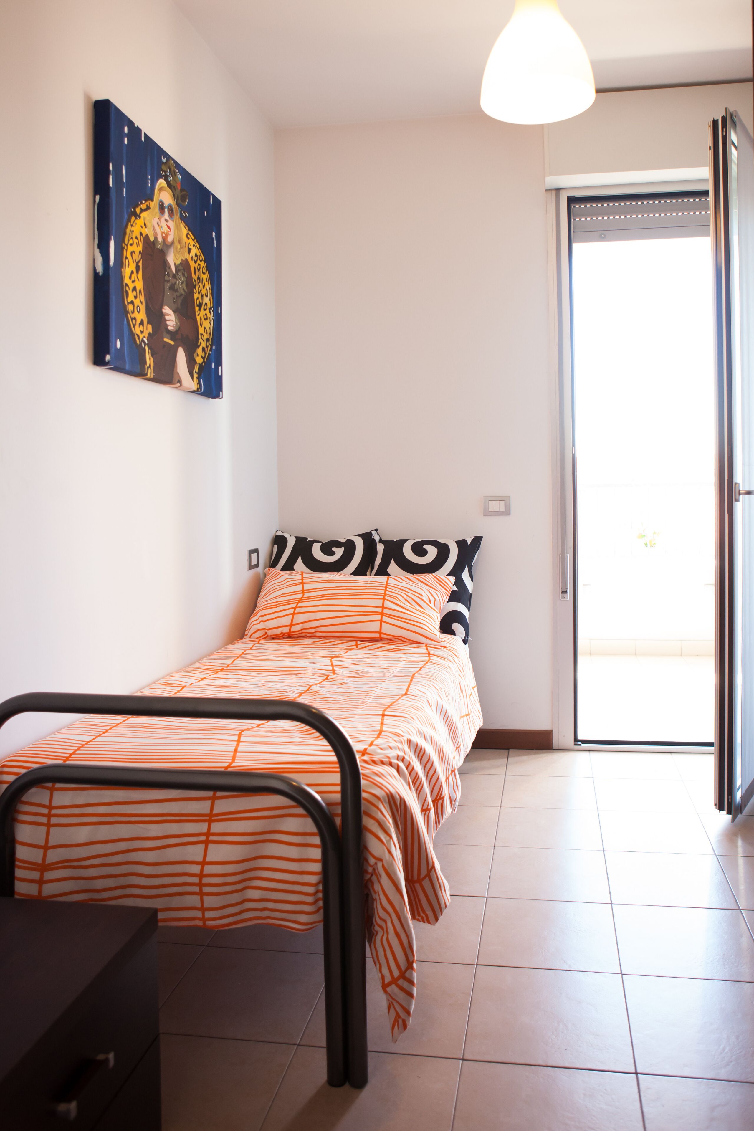A bedroom with a bed, a desk, and a door leading to a balcony.