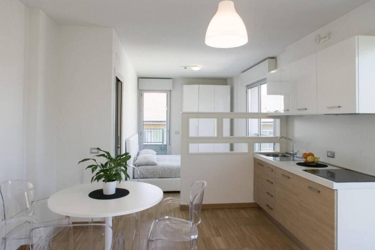 A modern kitchen with white cabinets, a round dining table with clear chairs, and a hanging pendant light.