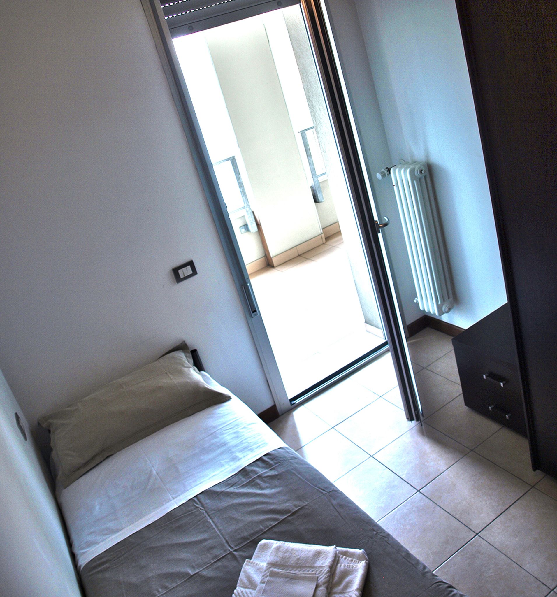 Une chambre avec un lit, un radiateur et une porte donnant sur un balcon.
