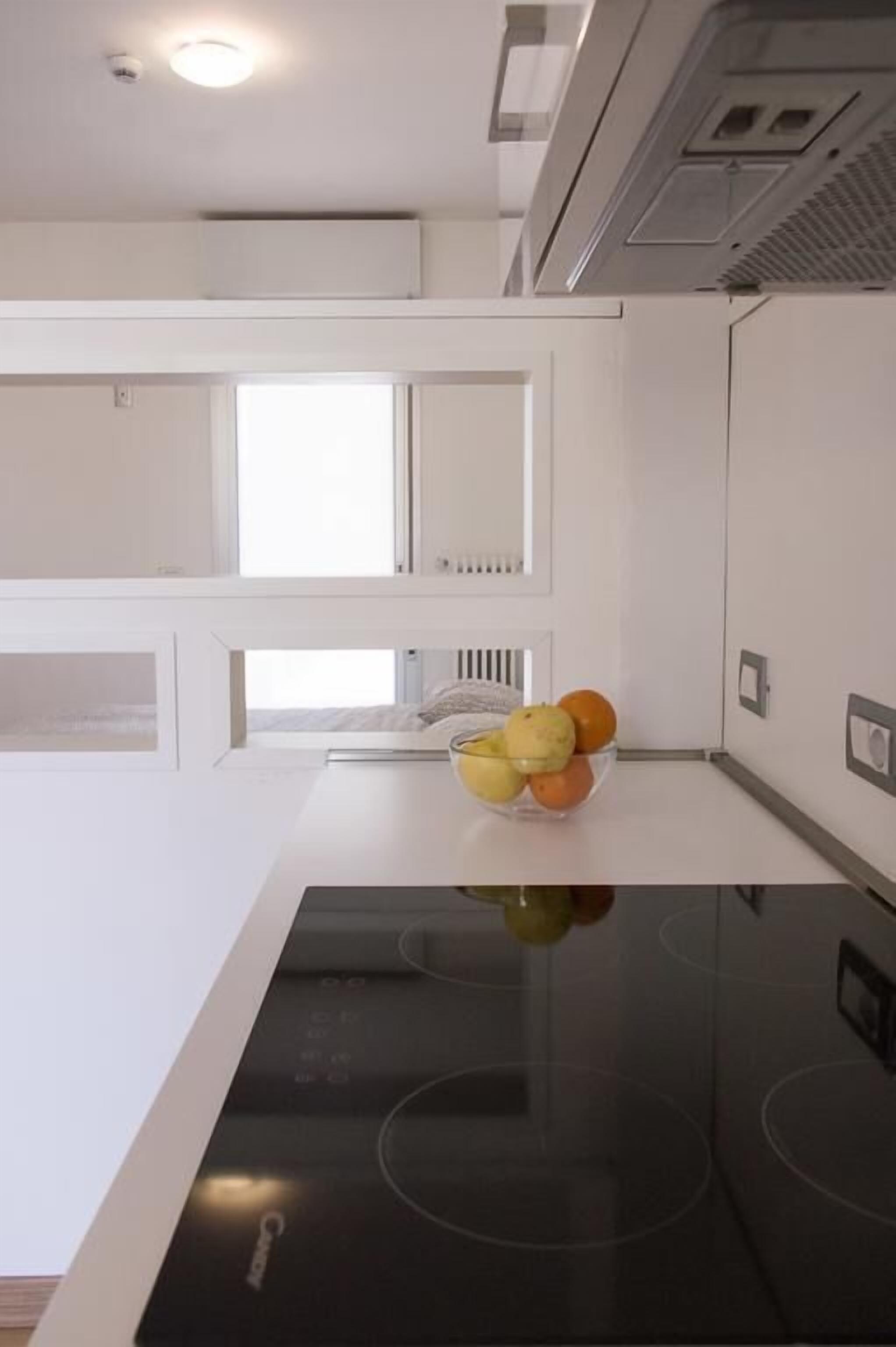 Une cuisine moderne avec des meubles blancs, une plaque de cuisson à induction noire et un saladier de fruits posé sur le plan de travail.