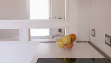 Une cuisine moderne avec des meubles blancs, une plaque de cuisson à induction noire et un saladier de fruits posé sur le plan de travail.