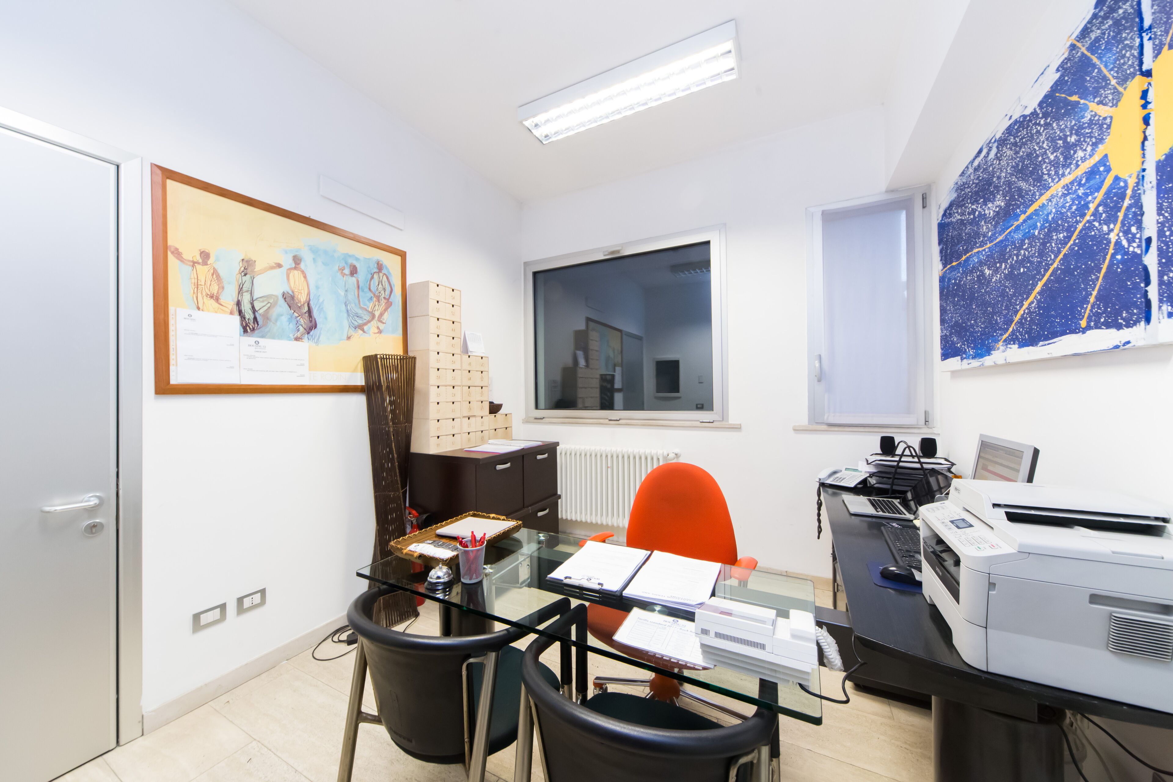 Ein modernes Büro mit einem Glastisch, einem Drucker und einem großen Fenster.