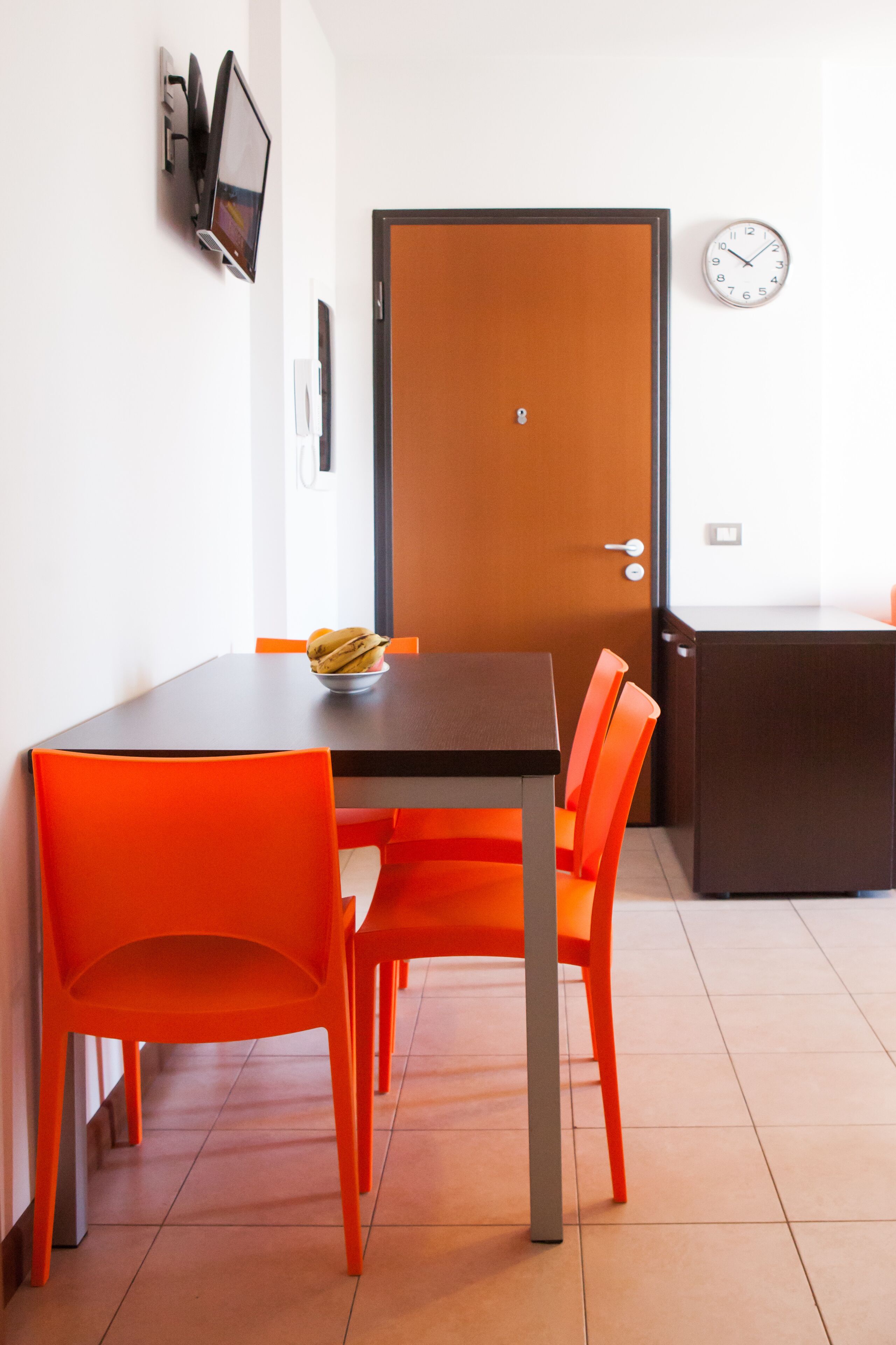 Un coin repas comprenant une table et des chaises, une porte, une horloge et un petit meuble.