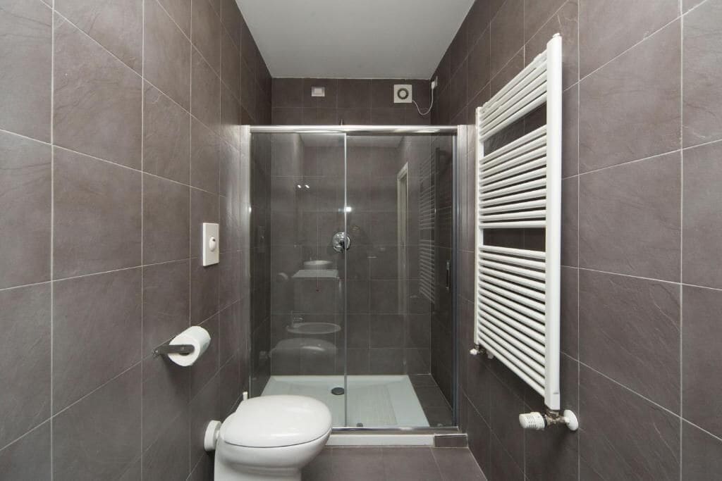 A modern bathroom with a glass-enclosed shower, a toilet, and a white radiator.