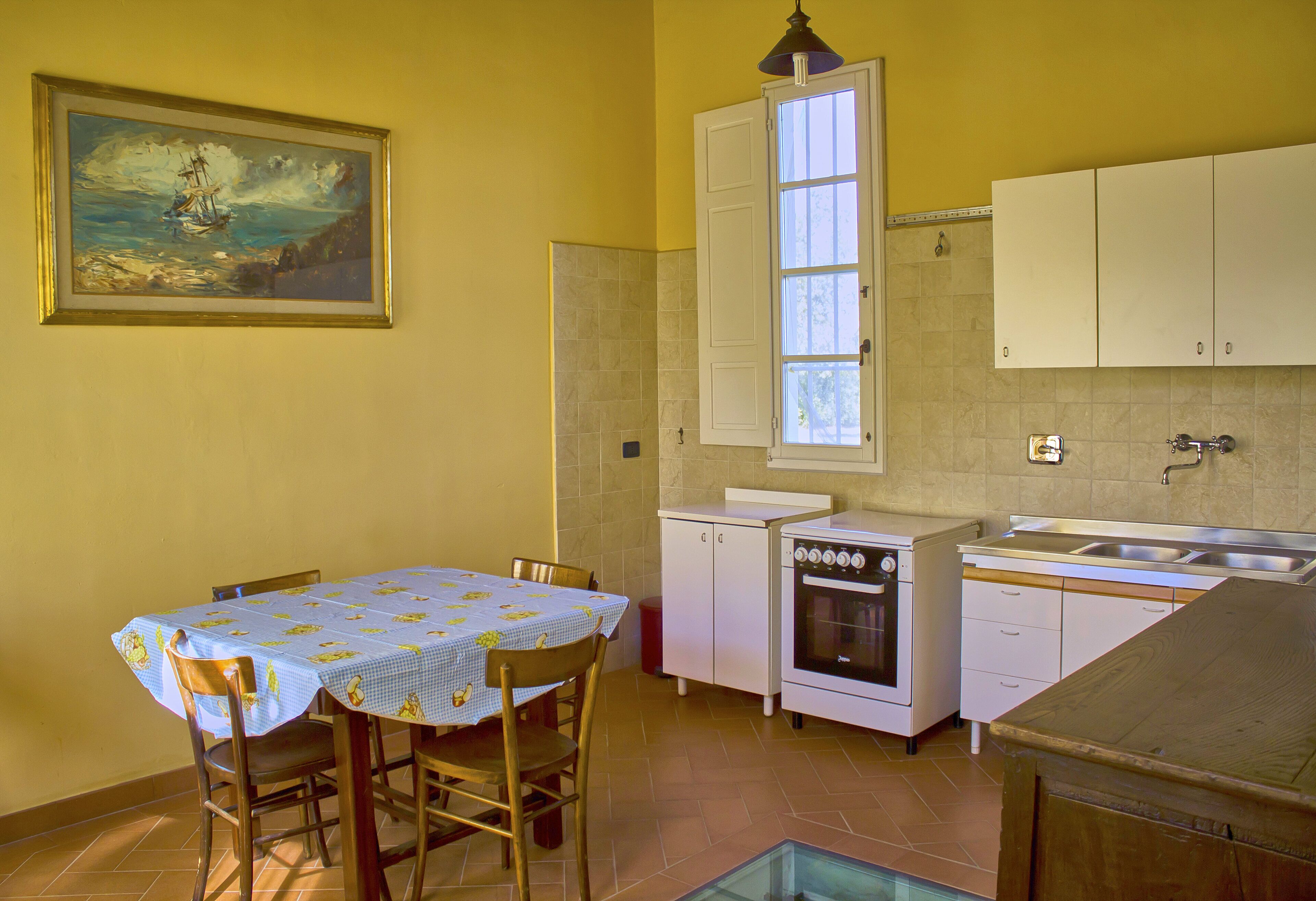 Une cuisine de taille réduite avec des meubles blancs, une cuisinière et une fenêtre au-dessus de l’évier.