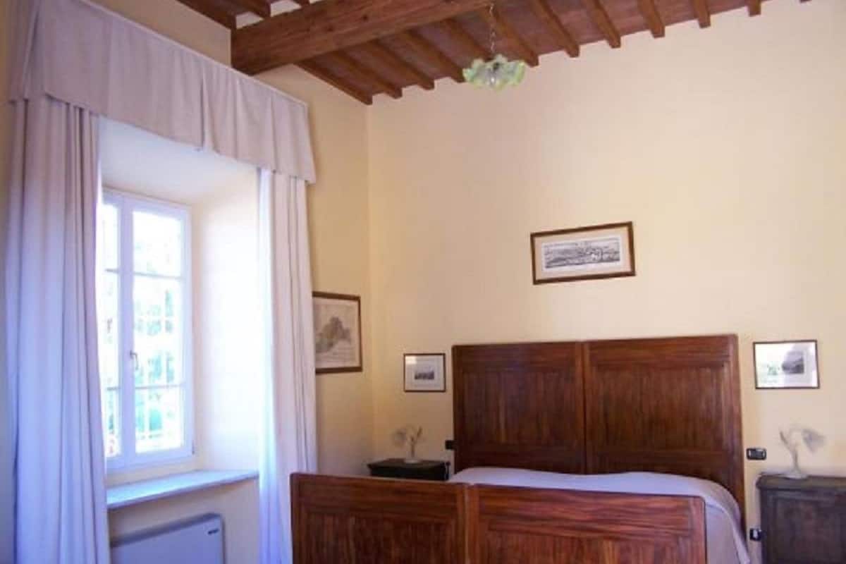 Ein Schlafzimmer mit einem hölzernen Bett, einem Fenster mit Vorhängen und einer Heizung.