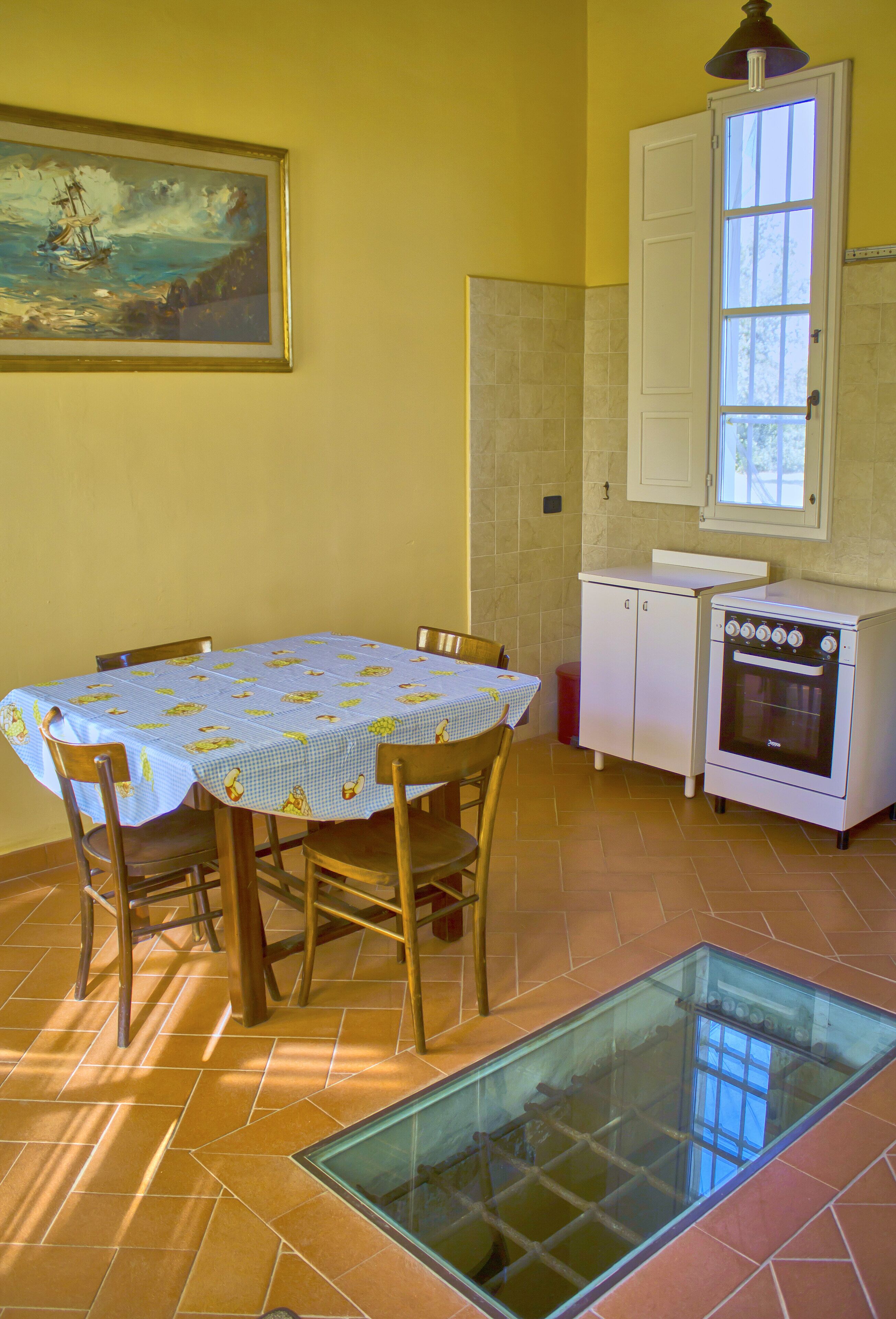 A kitchen with a dining table, chairs, a stove, cabinets, a window, and a painting on the wall.