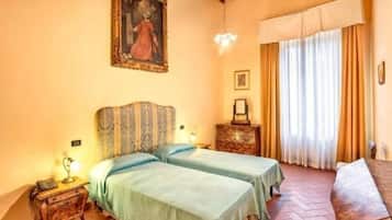 A room with two beds, a wooden headboard, a small table, a bench, and a painting on the wall.